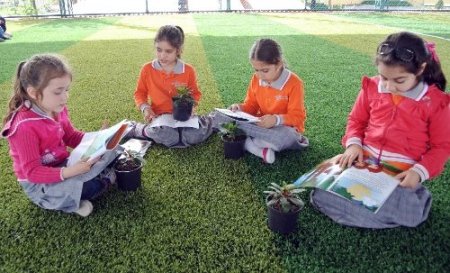 Öğrenciler çiçeklere kitap okuyor